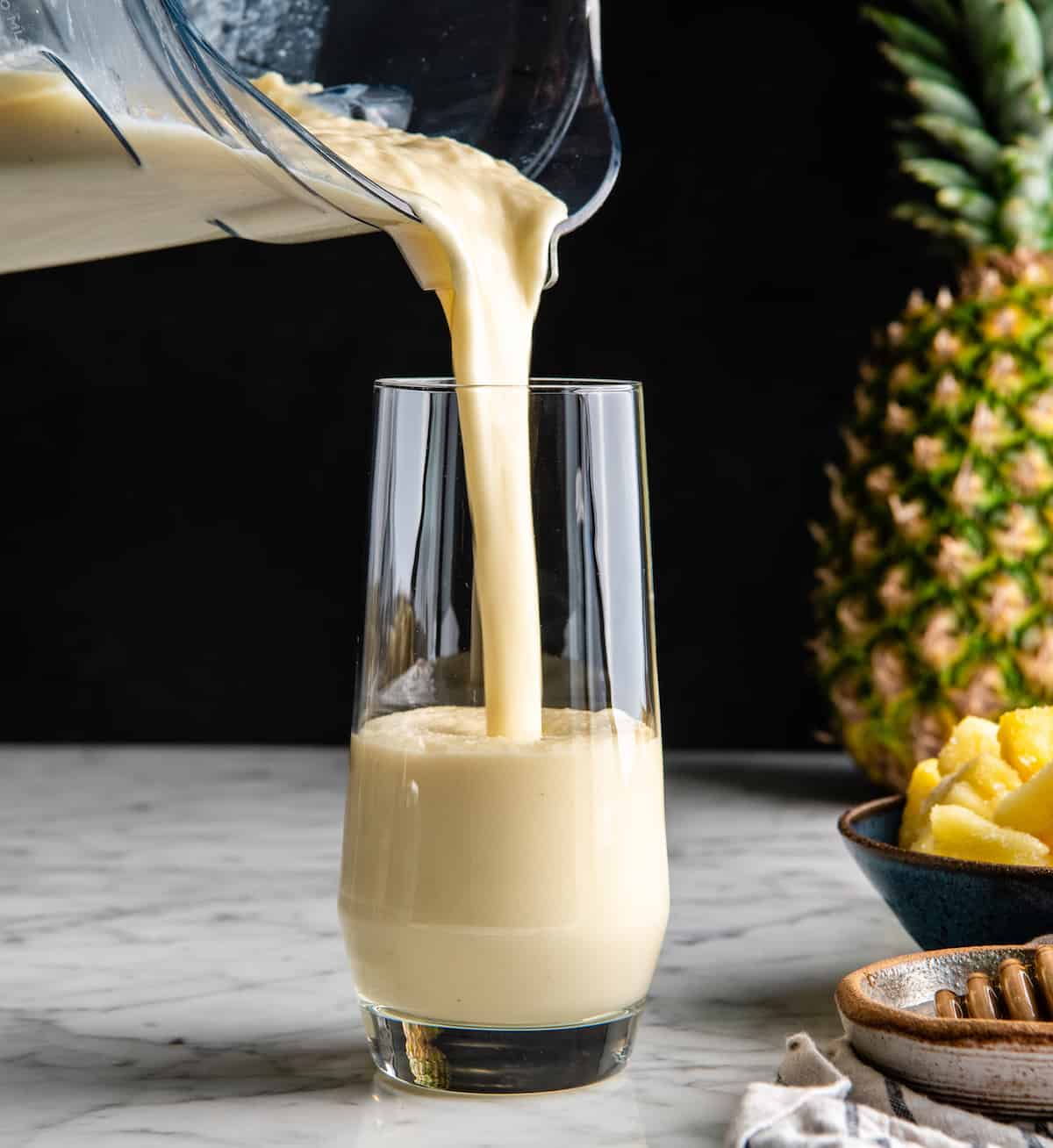This healthy Pineapple Smoothie recipe is easy to make with only 5 ingredients in 5 minutes! One sip of this pineapple banana smoothie will make you feel like you're on a tropical island, it's like a beach vacation in a glass! Plus it's dairy-free! #pineapple #smoothie #pineapplesmoothie #banana #joyfoodsunshine #smoothierecipe front view of a pineapple smoothie being poured into a glass
