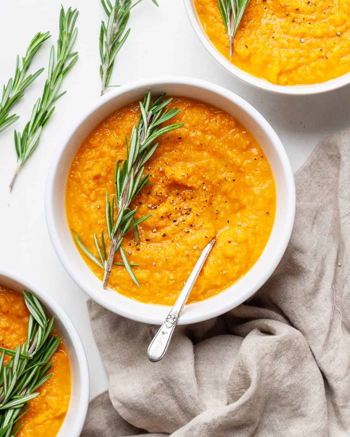 Roasted Root Vegetable Soup with butternut squash, sweet potatoes, parsnips & carrots! The perfect healthy fall soup recipe! Gluten-Free, dairy-free, vegan, & paleo! #vegetablesoup #soup #vitamix #roastedvegetables #sweetpotato #butternutsquash #vegan #paleo #whole30 #glutenfree #dairyfree #sugarfree a bowl of roasted vegetable soup garnished with fresh rosemary