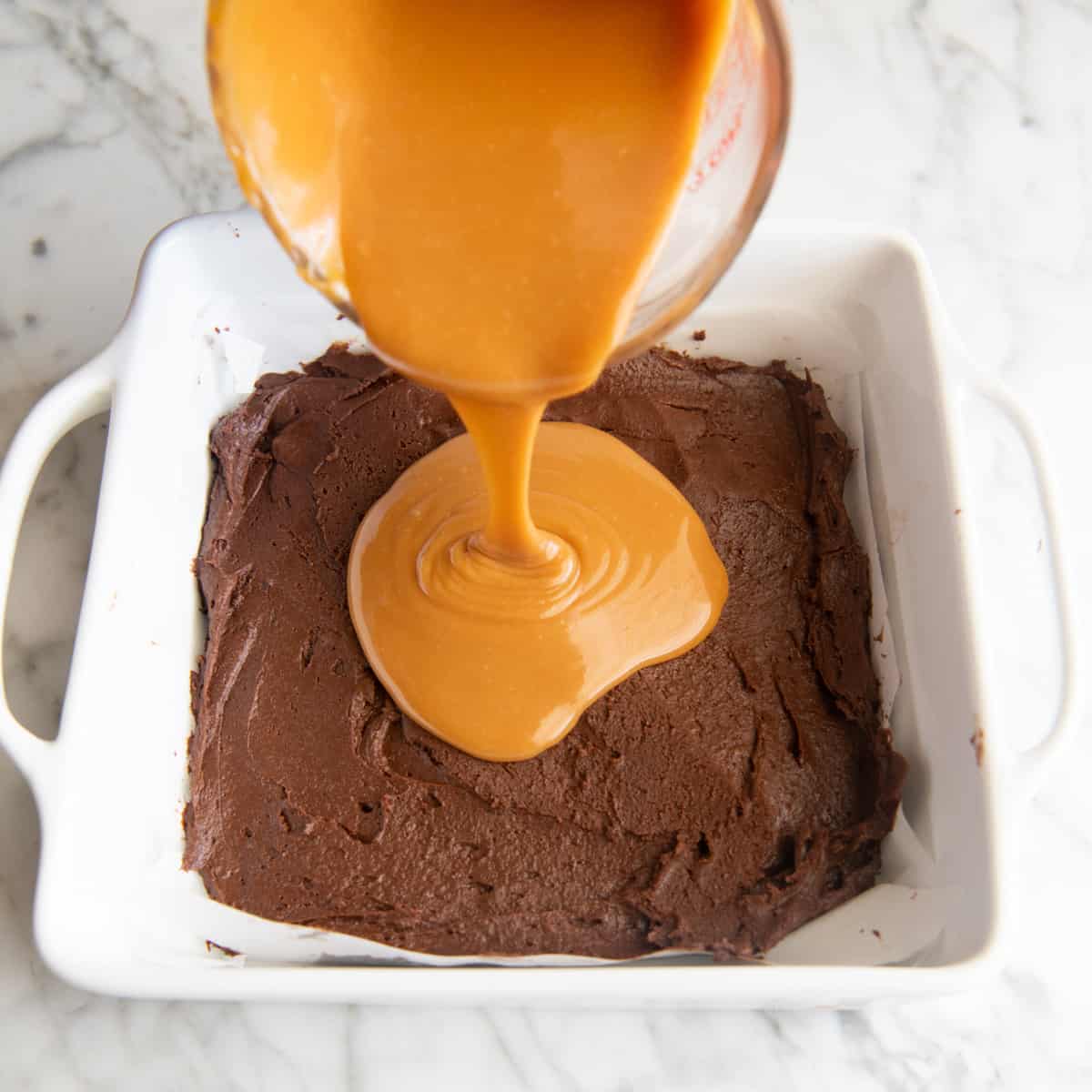 caramel pouring over the bottom layer of the caramel brownies batter