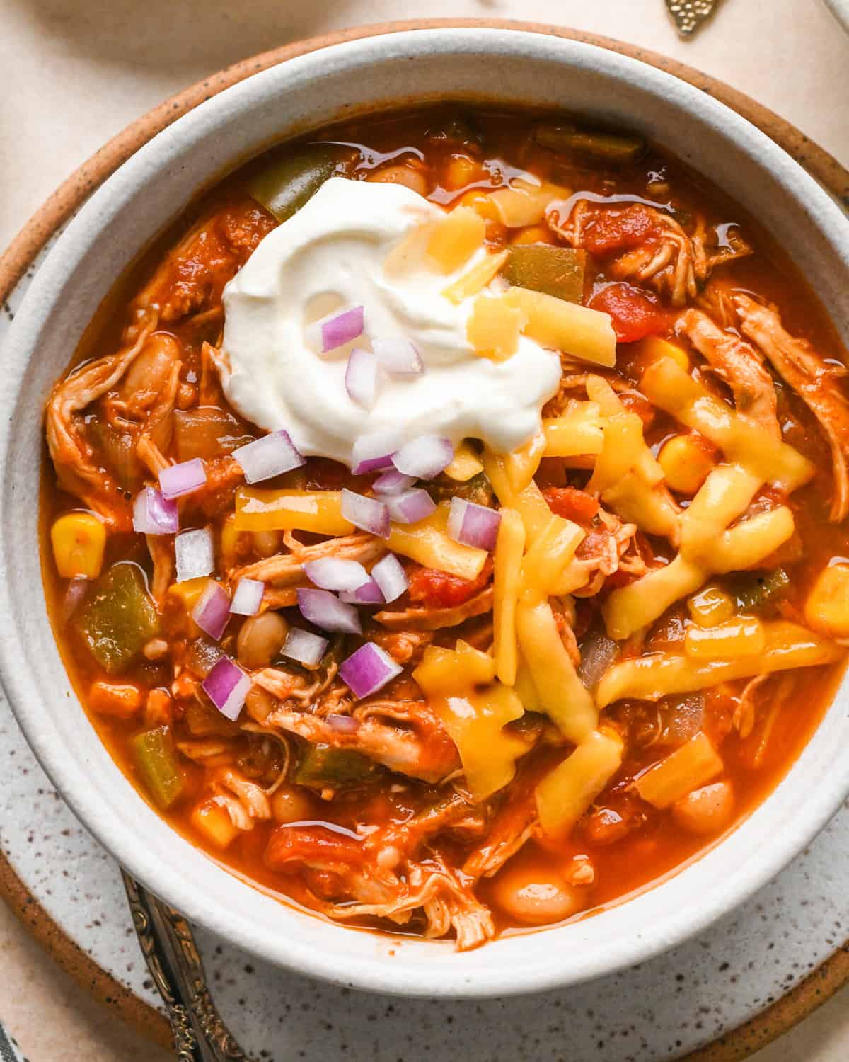 a bowl of Slow Cooker Chicken Chili topped with shredded cheese, sour cream and red onion.