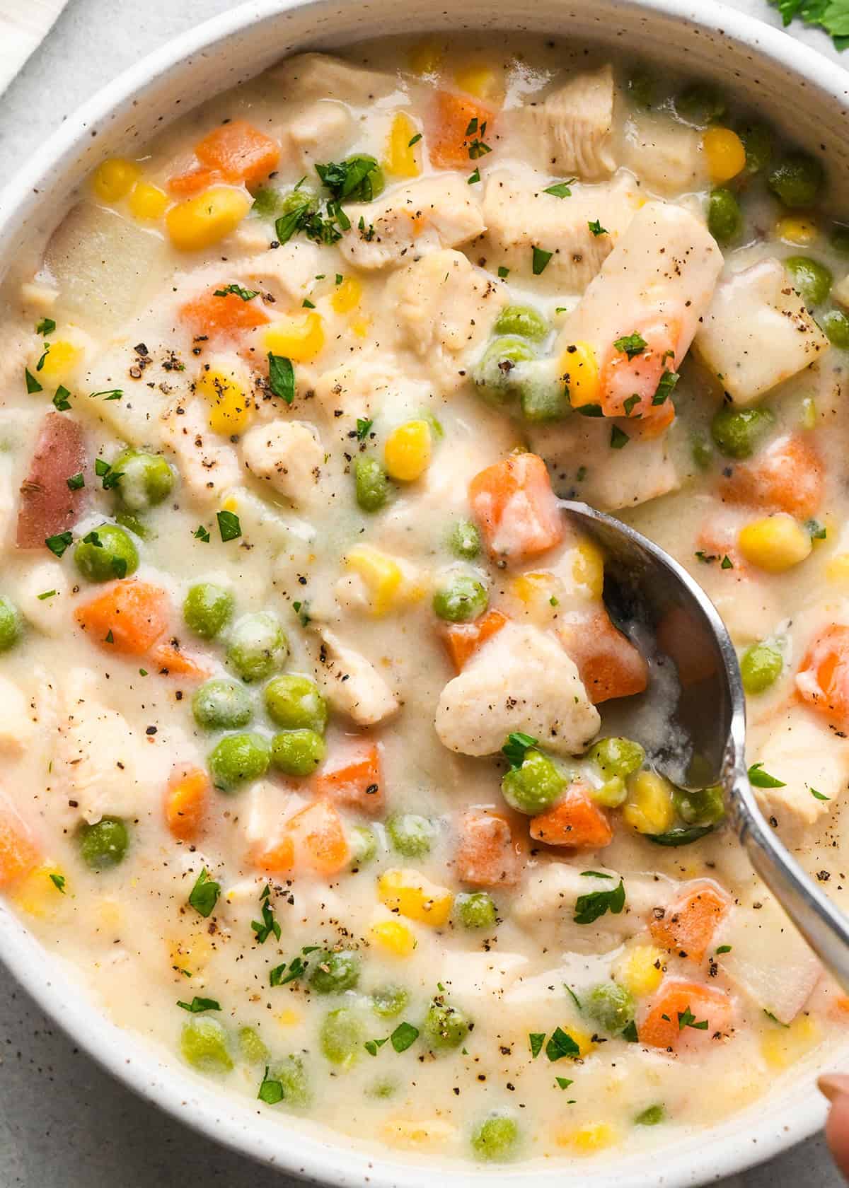 This lightened-up Slow Cooker Chicken Pot Pie Soup only takes 10 minutes of prep! This recipe is made from scratch {NO canned soups} and sure to please even the pickiest eaters! Plus it's gluten-free! #slowcooker #chickenpotpiesoup #chickensoup #easydinner #maindish #healthyrecipe a spoon taking a scoop of chicken pot pie soup in a bowl