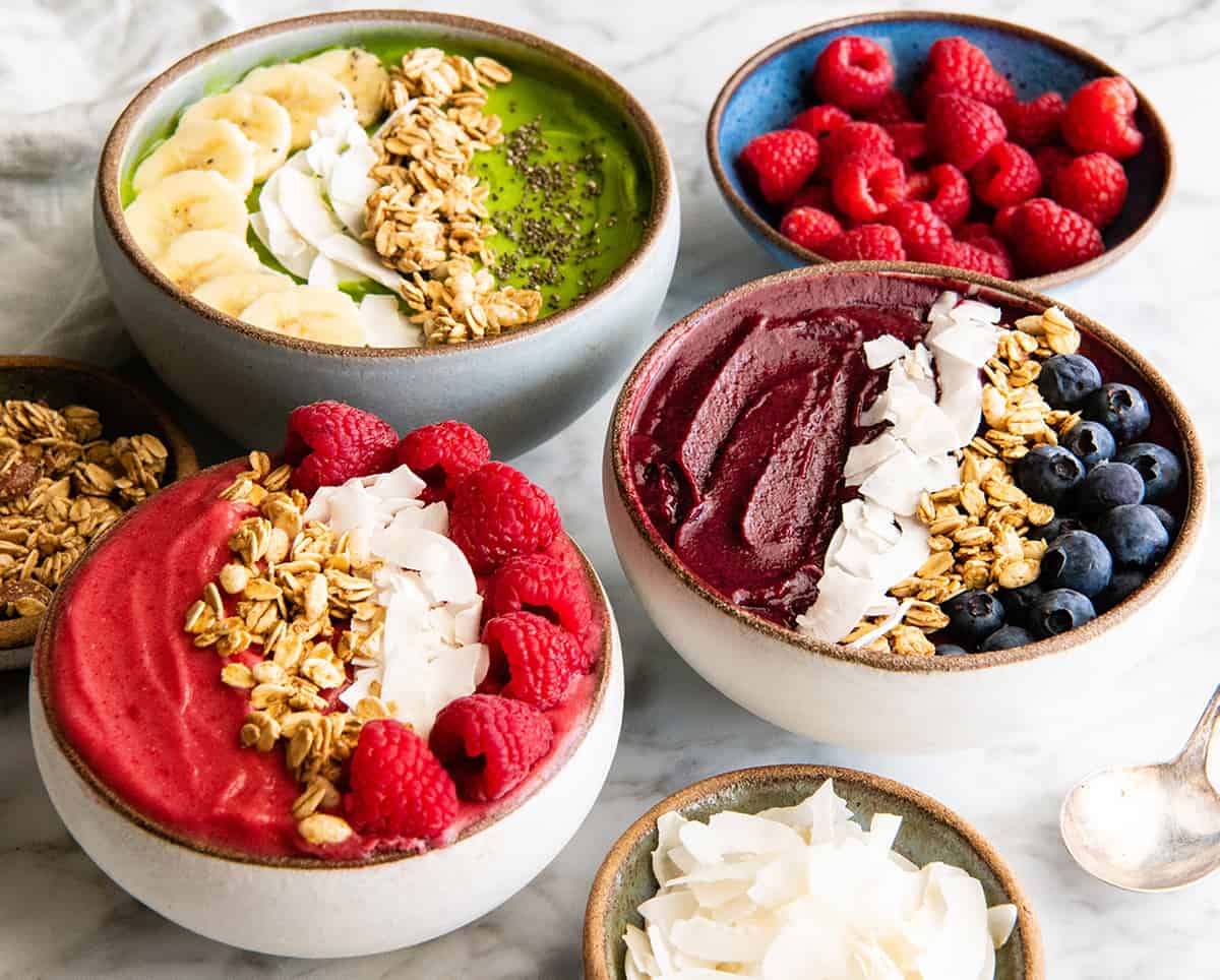 Follow our step-by-step photos & video to learn how to make the BEST easy & healthy smoothie bowl recipe (3 varieties) with 5 ingredients in 5 minutes! Smoothie bowls make the best breakfast, brunch or snack, and you can save so much money making them at home! Paleo, dairy-free and vegan-friendly. front view of three smoothie bowls, one green one pink and one purple