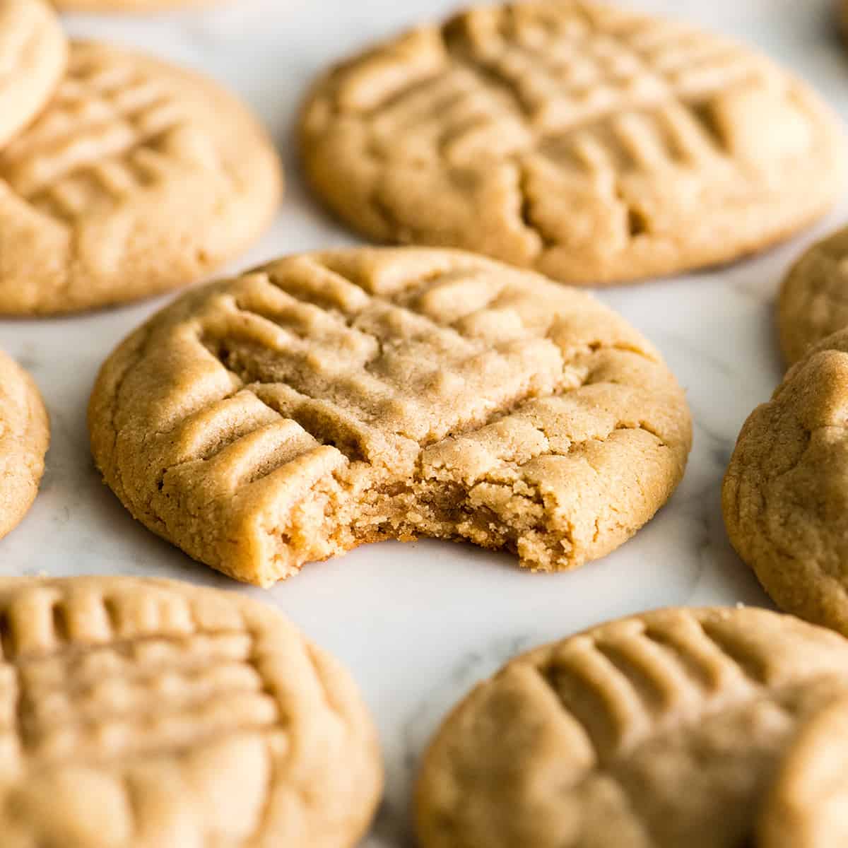 This is the BEST peanut butter cookie recipe ever! These classic, soft peanut butter cookies are easy to make, loaded with peanut butter, and will definitely become your new favorite peanut butter cookie recipe! Learn how to make peanut butter cookies by following our step-by-step instructions and watching the video! #peanutbuttercookies #cookies #peanutbutter #dessert front view of a peanut butter cookie with a bite taken out of it