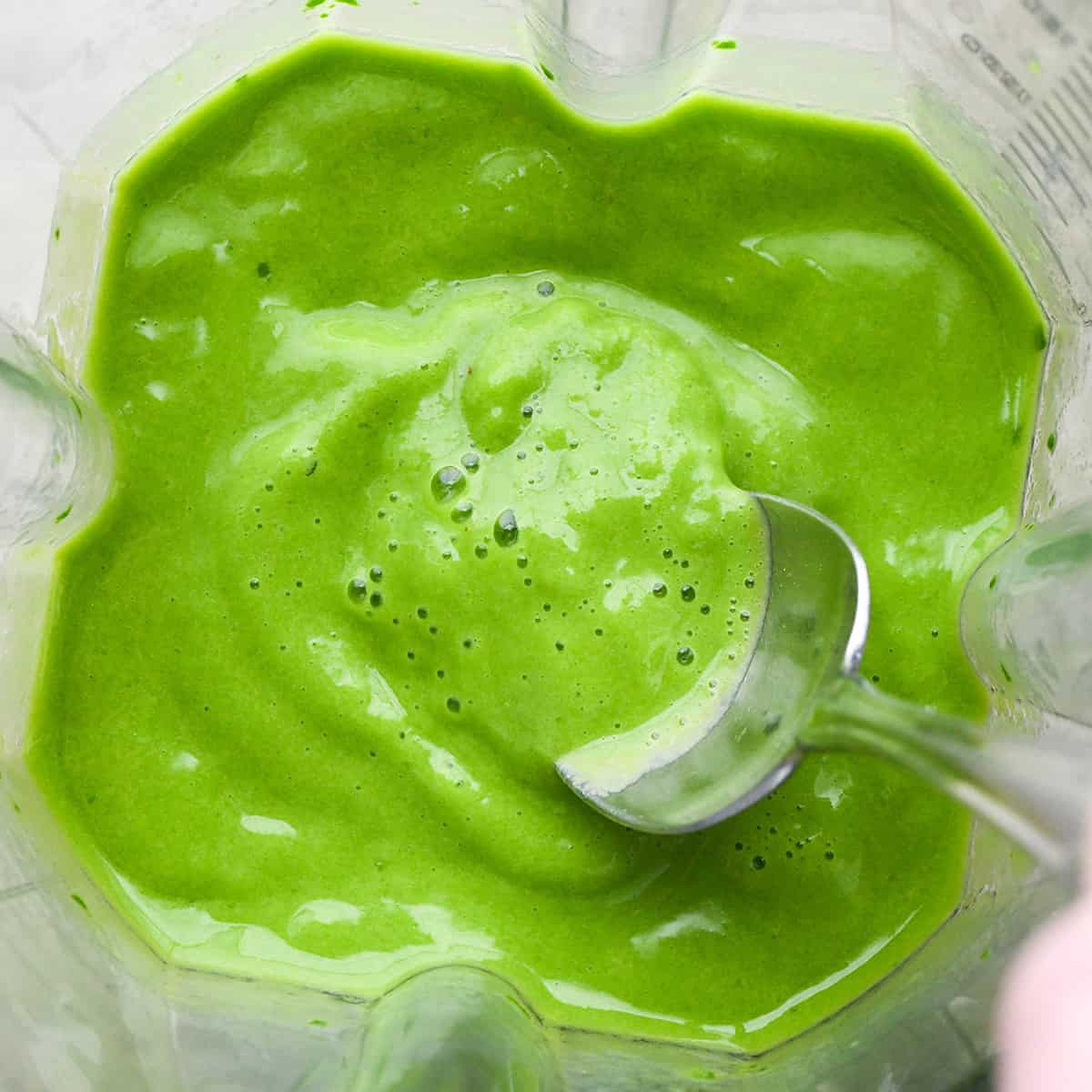 Spinach Smoothie in a blending container after blending with a spoon