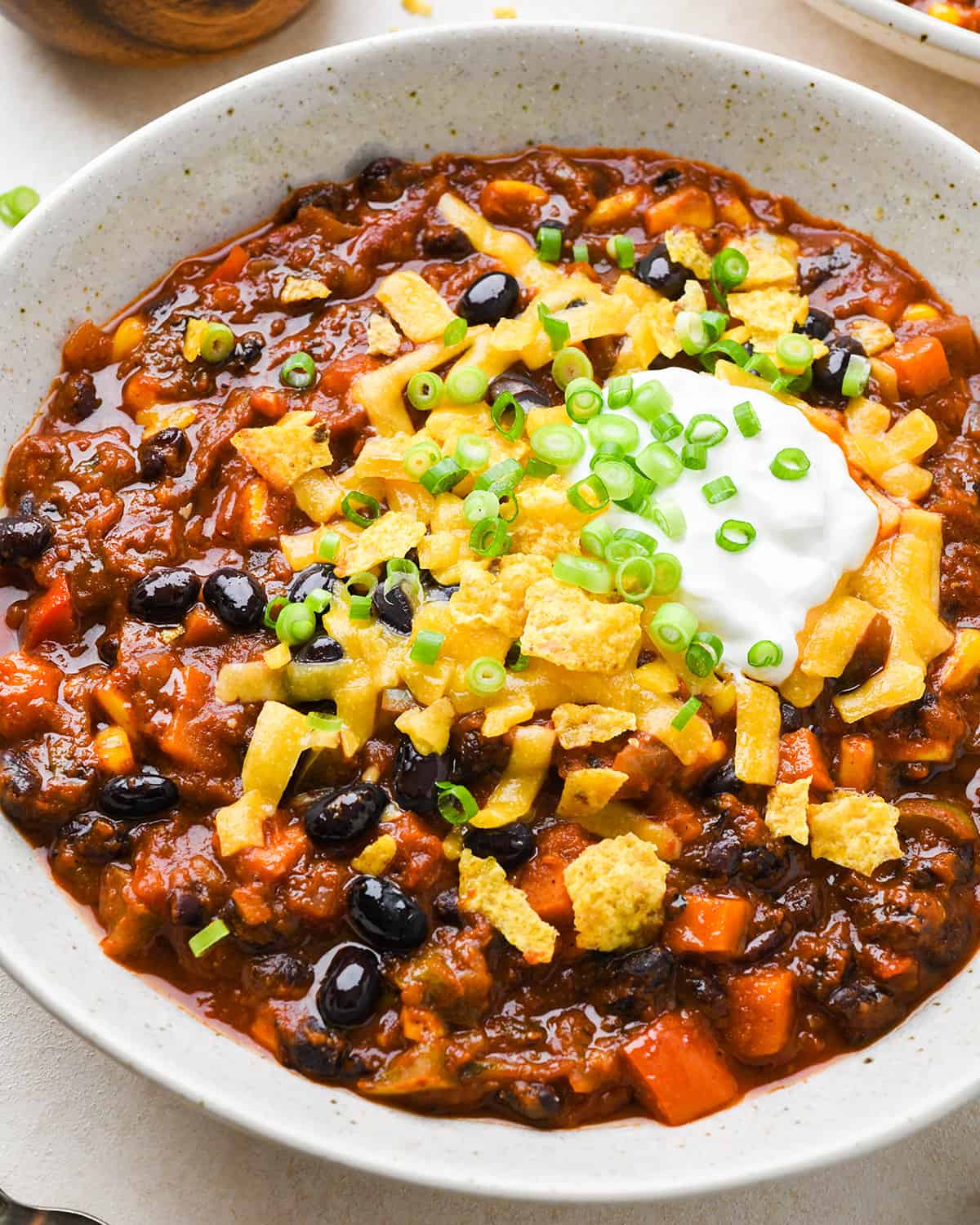 a bowl of Vegetarian Chili with sour cream, cheese, chips and chives.