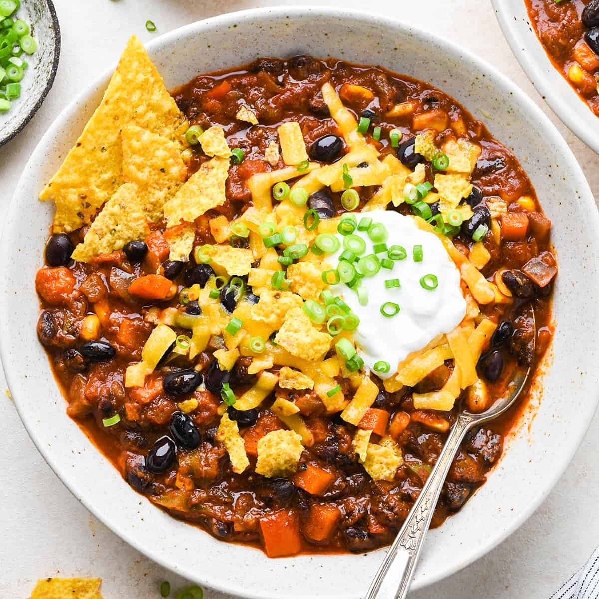 a bowl of Vegetarian Chili with sour cream, cheese, chips and chives.