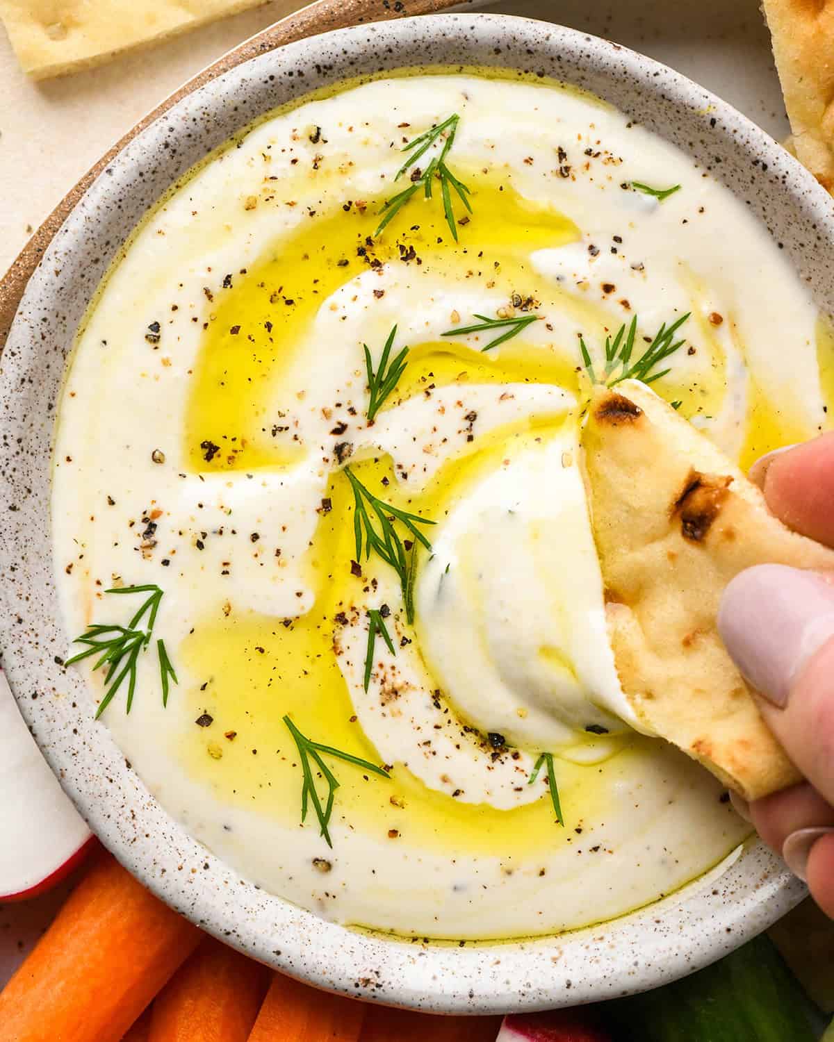 a piece of bread being dipped into a bowl of Whipped Feta Cheese Dip