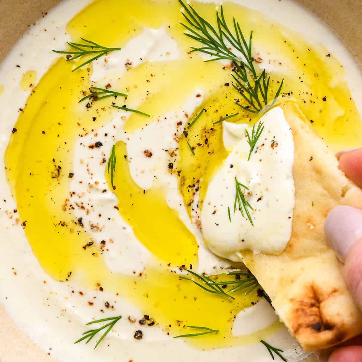 a piece of bread being dipped into whipped feta cheese dip