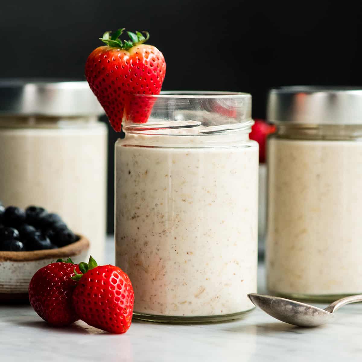 Easy Overnight Oats with Yogurt are a great healthy high-protein breakfast! This recipe only takes 6 ingredients and 5 minutes to prepare! Plus it's no-cook, gluten-free and can easily be made dairy-free! #overnightoats #oatmeal #greekyogurt #yogurt #glutenfree #breakfast #healthyrecipe #mealprep front view of three glass jars of Yogurt Overnight Oats with berries on top and around them